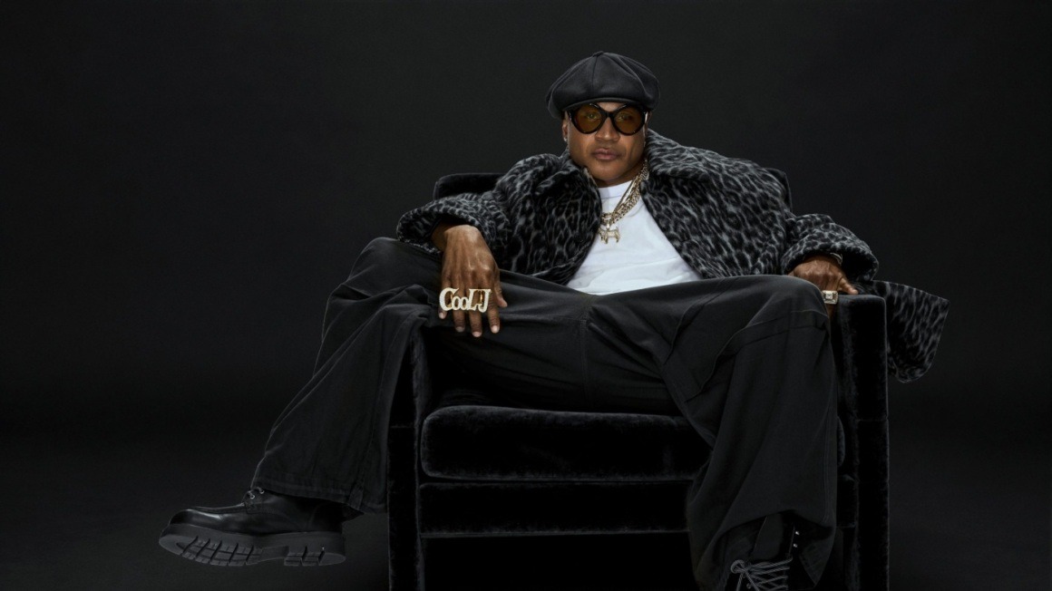LL COOL J seated in a black chair wearing sunglasses and a black cap