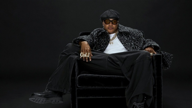 LL COOL J seated in a black chair wearing sunglasses and a black cap